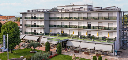 Außenansicht eines modernen, mehrstöckigen Hotels mit Sonnenterrasse, verglasten Balkonen und einem gepflegten Garten.